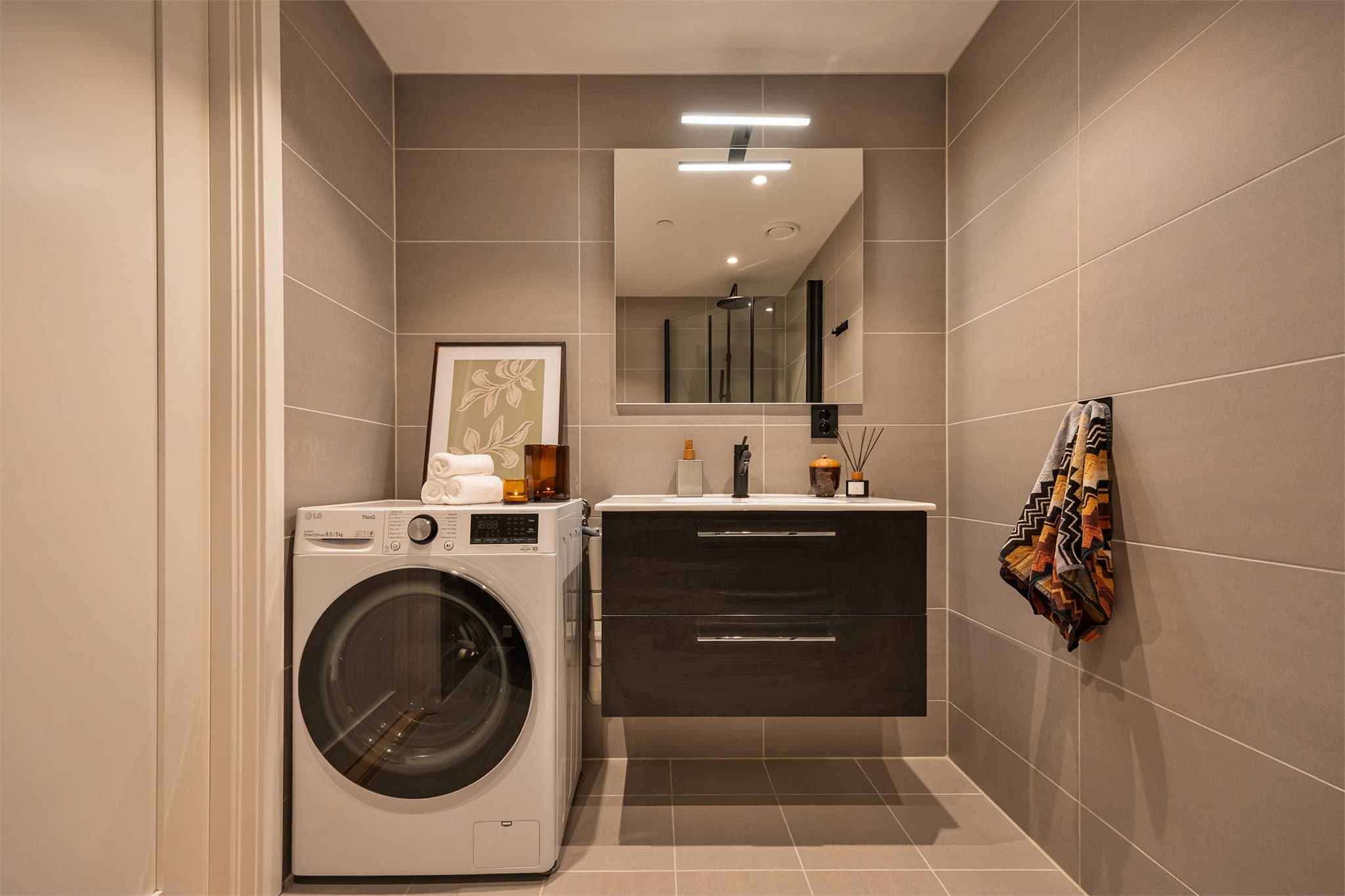 Badet er innredet med helservant på skuffeseksjon, dusjhjørne med regnfallsdusj, vegghengt toalett og opplegg for vaskemaskin.