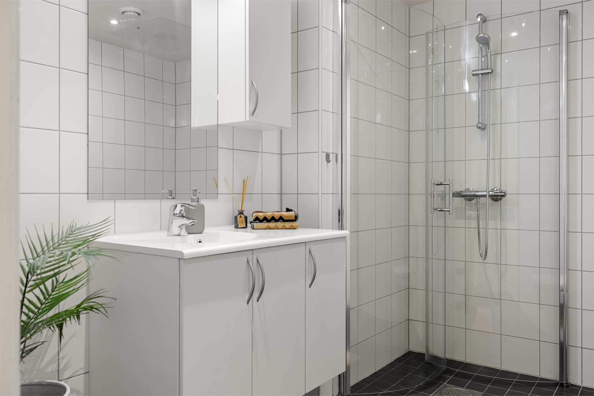 badet har servantinnredning, veggmontert toalett og dusjløsning med glassvegger.