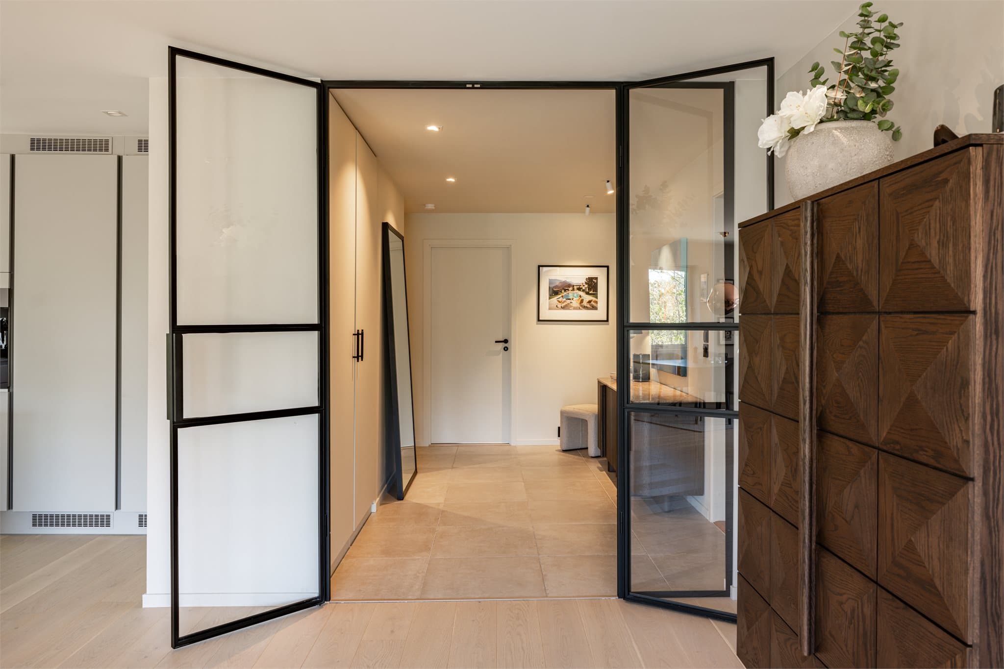 Leiligheten har en romslig og elegant entré. En vakker tofløyet glassdør åpner opp mot stuen og skaper en elegant overgang mellom rommene, samtidig som lys og romfølelse flyter harmonisk gjennom boligen.
