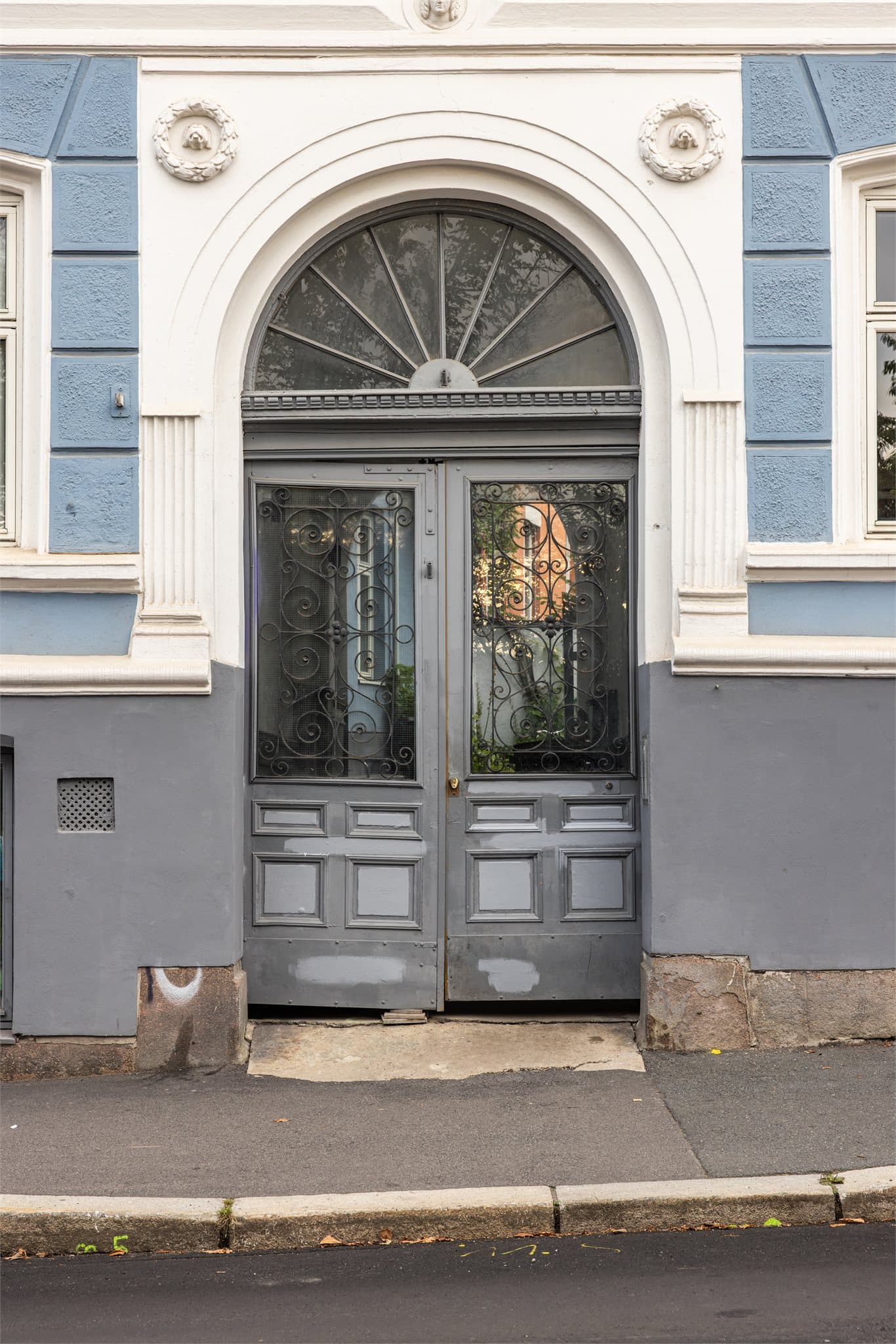 Innbydende inngangsparti med originale dobbeltdører, dekorative smijernsdetaljer og tidstypisk buet vindu.
