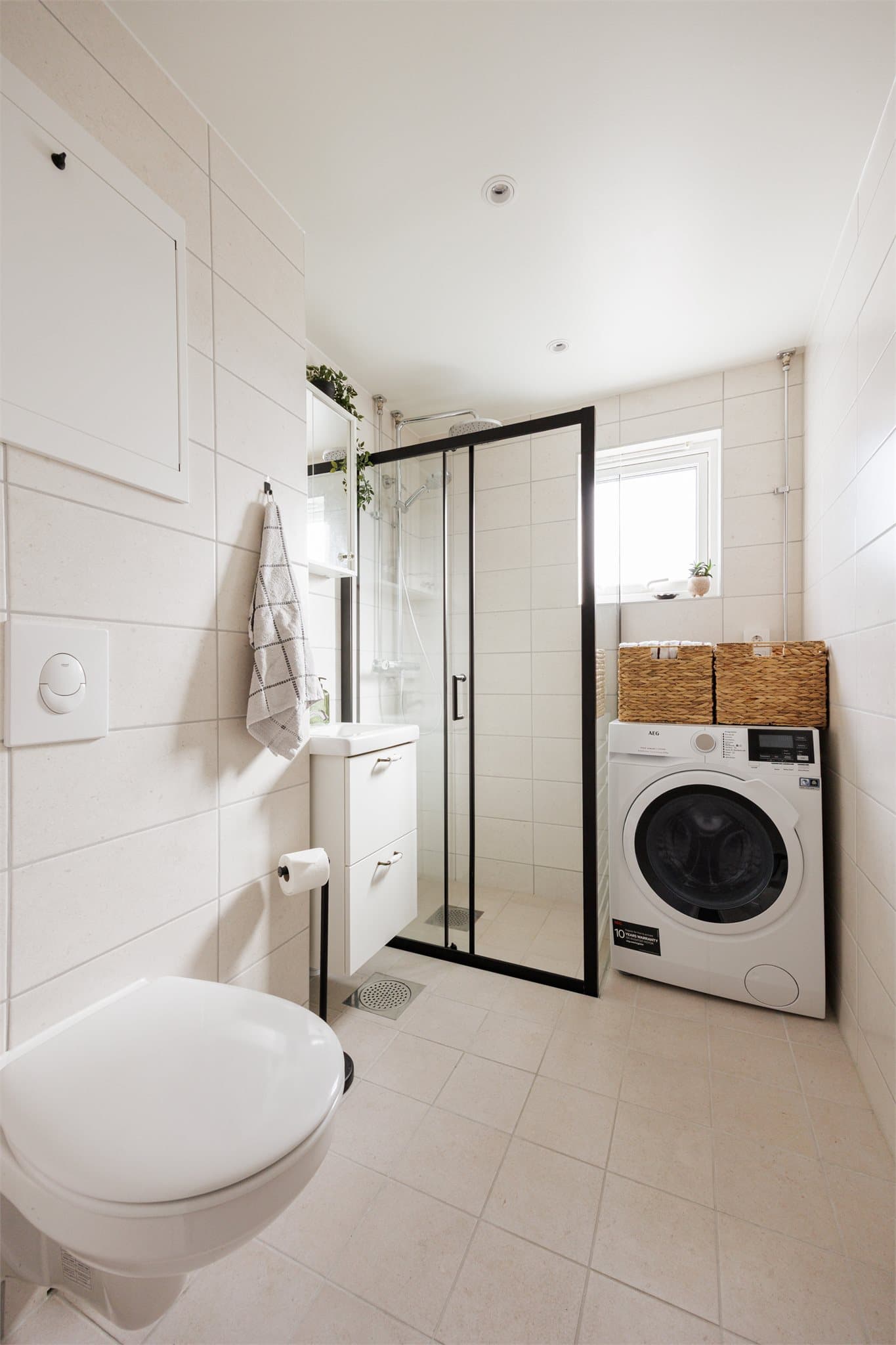 Dusj med dører i herdet glass, servant og vegghengt toalett med innebygget sisterne. Opplegg for vaskemaskin.