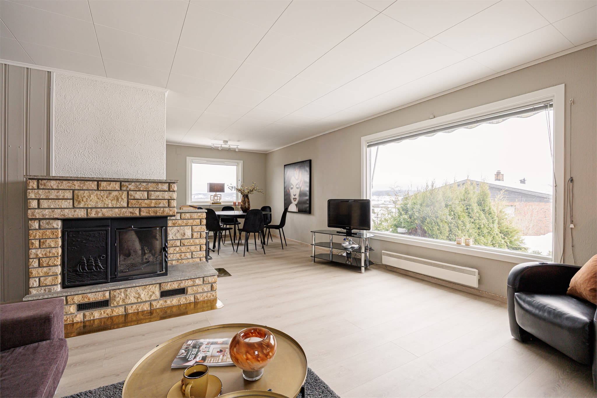 Lys stue med peis og store vindusflater som gir godt med naturlig lys og en åpen romfølelse.