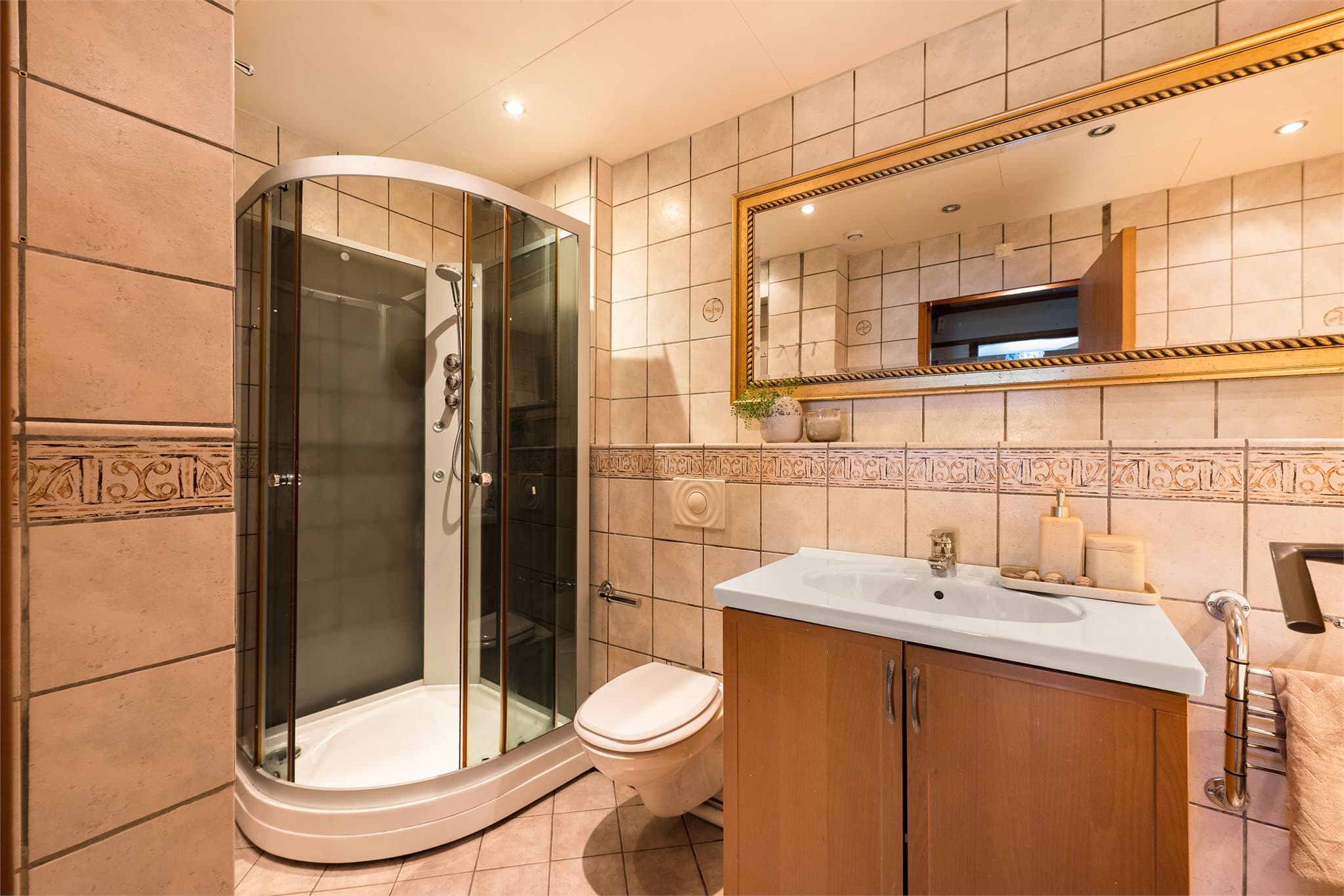 Badet er innredet med vegghengt toalett, dusjkabinett, helservant på underskap og hjørnebadekar.