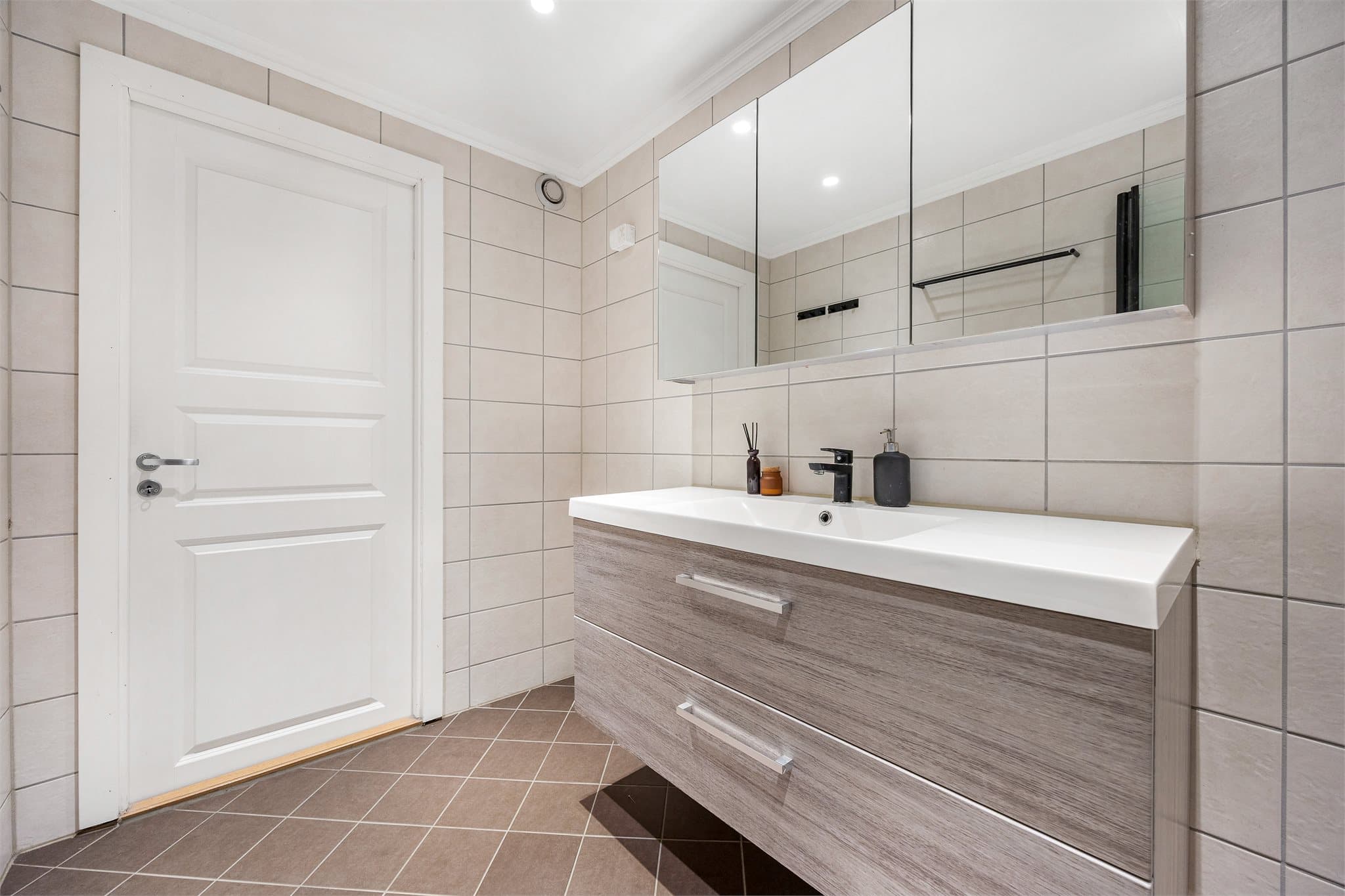 Badet er innredet med servantmøbel med glatte fronter og et stort speilskap. Det er varmekabler på gulvet.