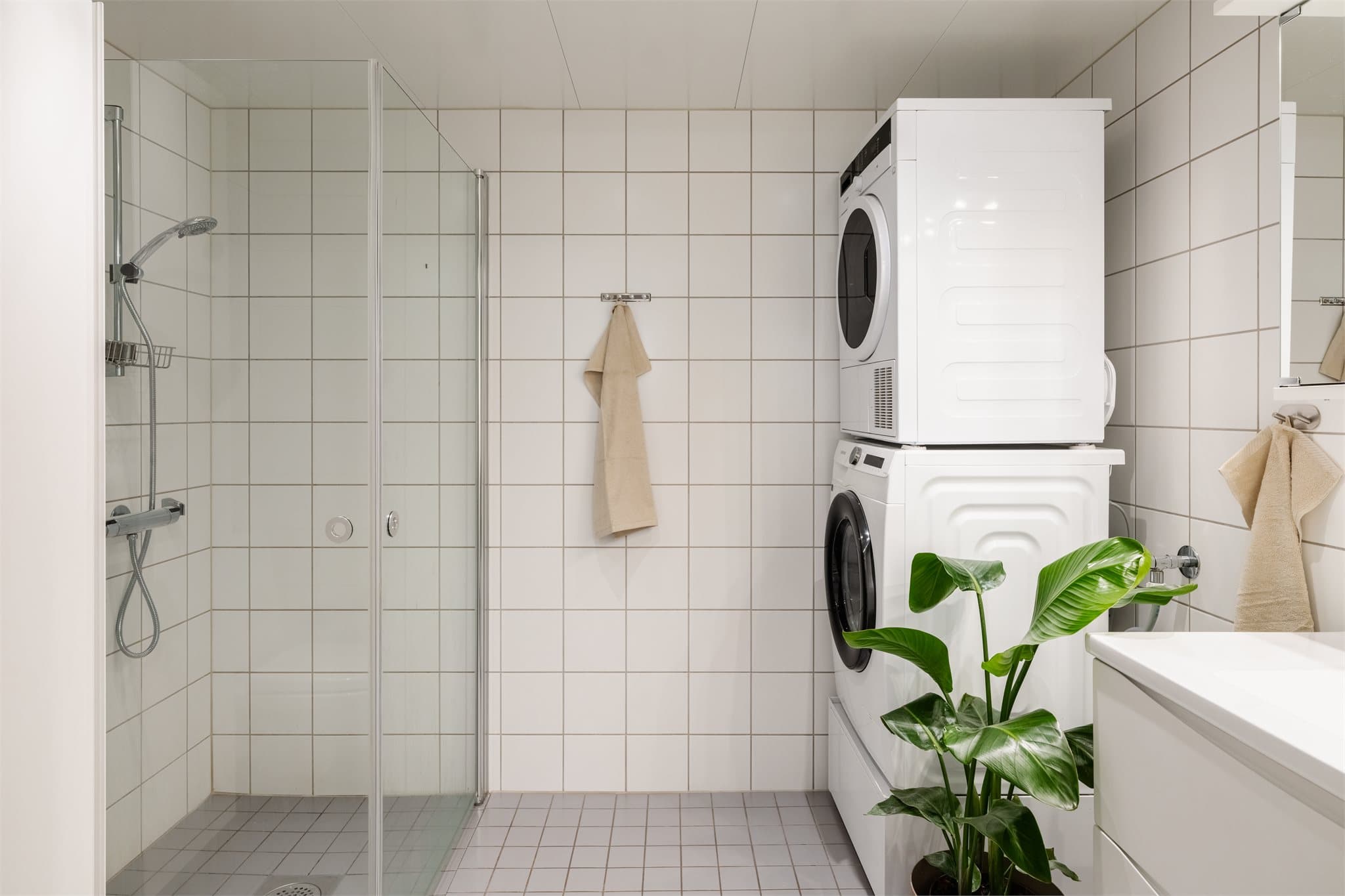Flislagt bad med varmekabler i gulvet, dusjhjørne og opplegg for vaskemaskin.