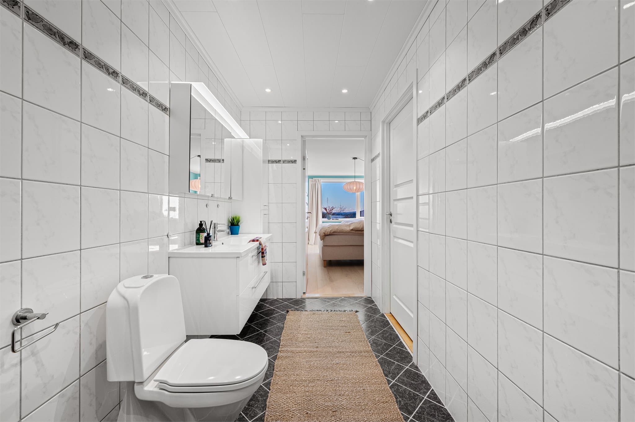 - Badet er innredet med toalett, heldekkende servant (fra 2023), speilskap og dusjhjørne -