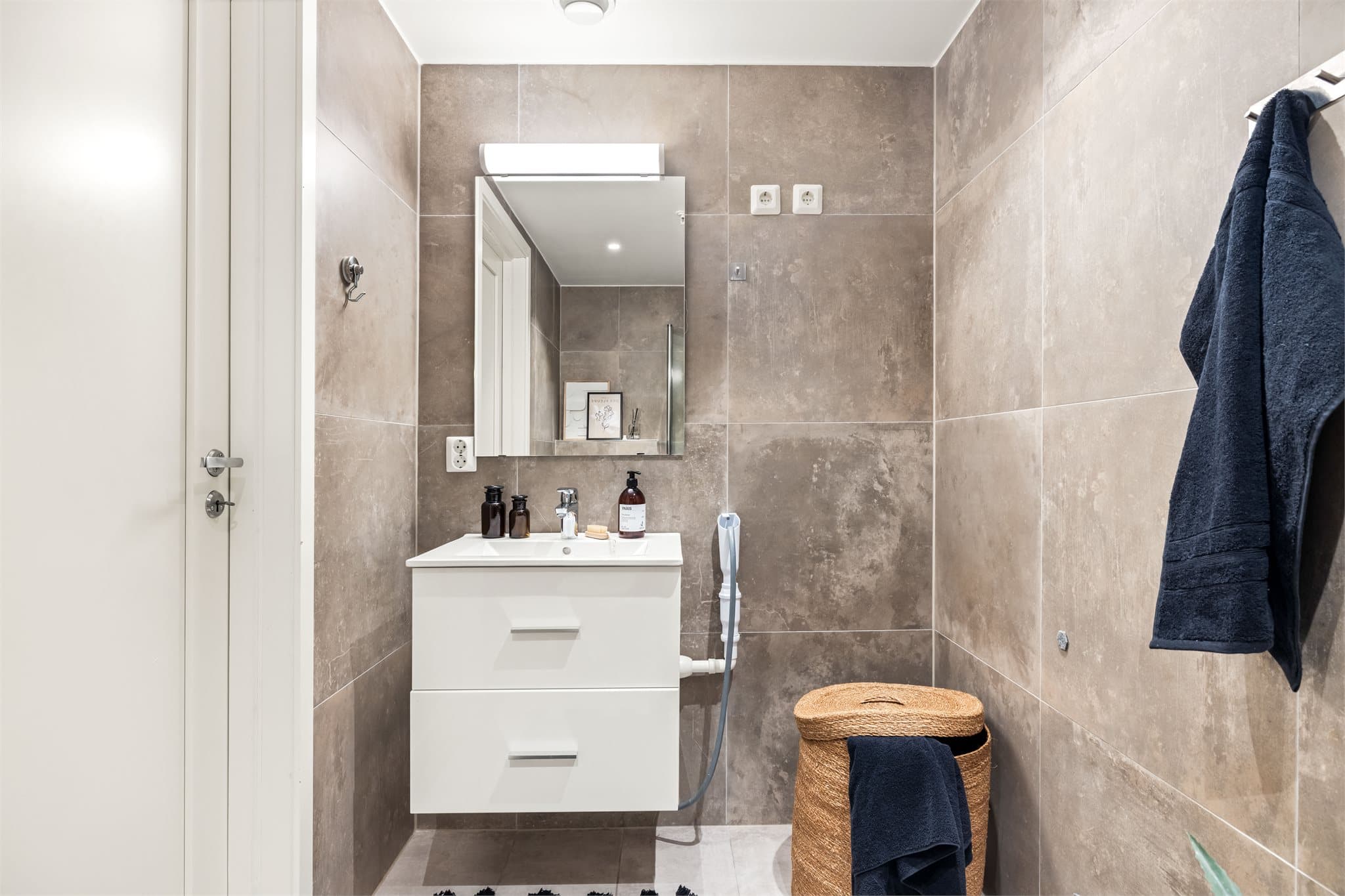 Badet er innredet med hvit servant med underskap, speil og opplegg for vaskemaskin.