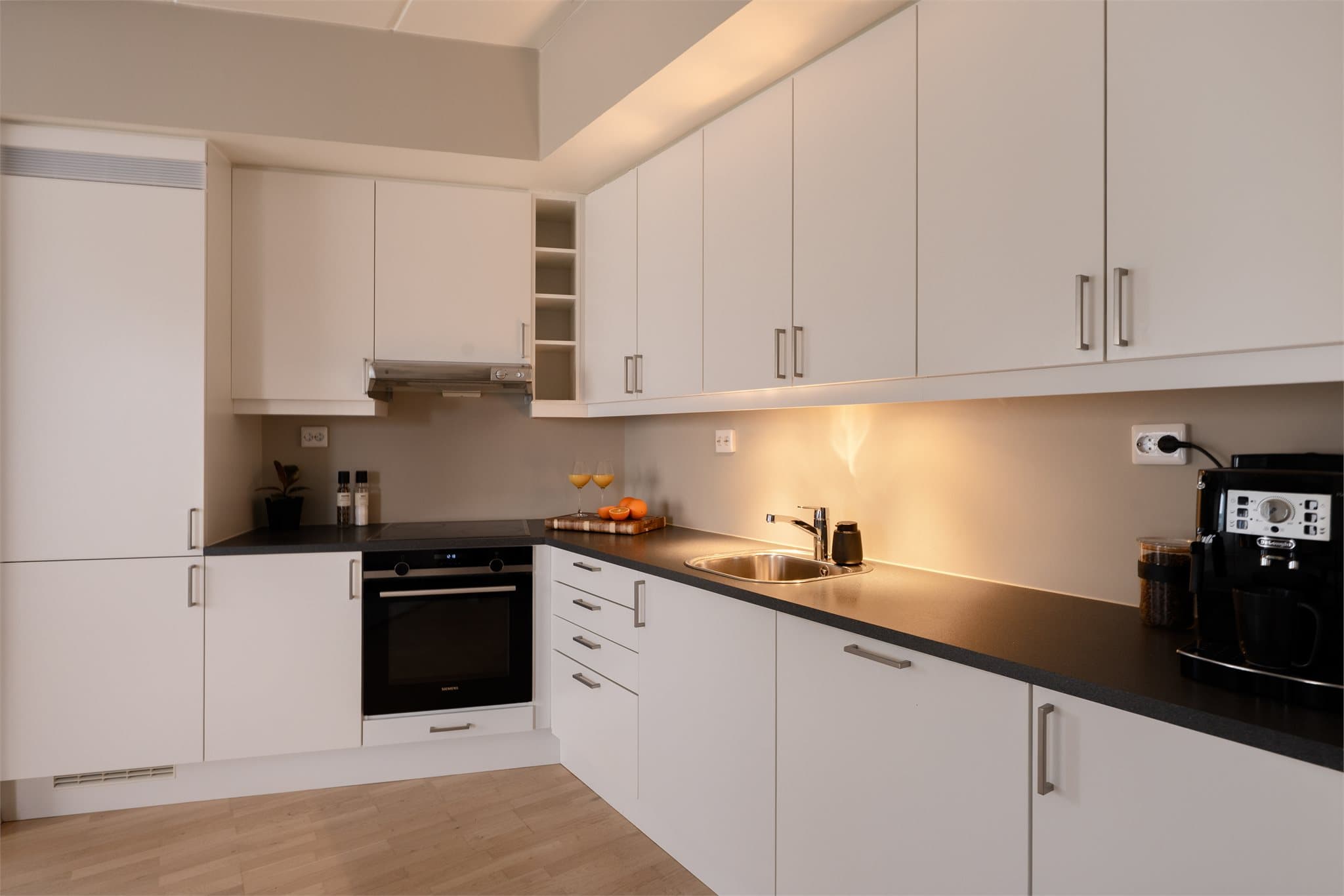 Tidløs kjøkkeninnredning fra Sigdal med glatte, fabrikklakkerte fronter og laminat benkeplate. Det er praktisk belysning under overskap som gir godt arbeidslys.