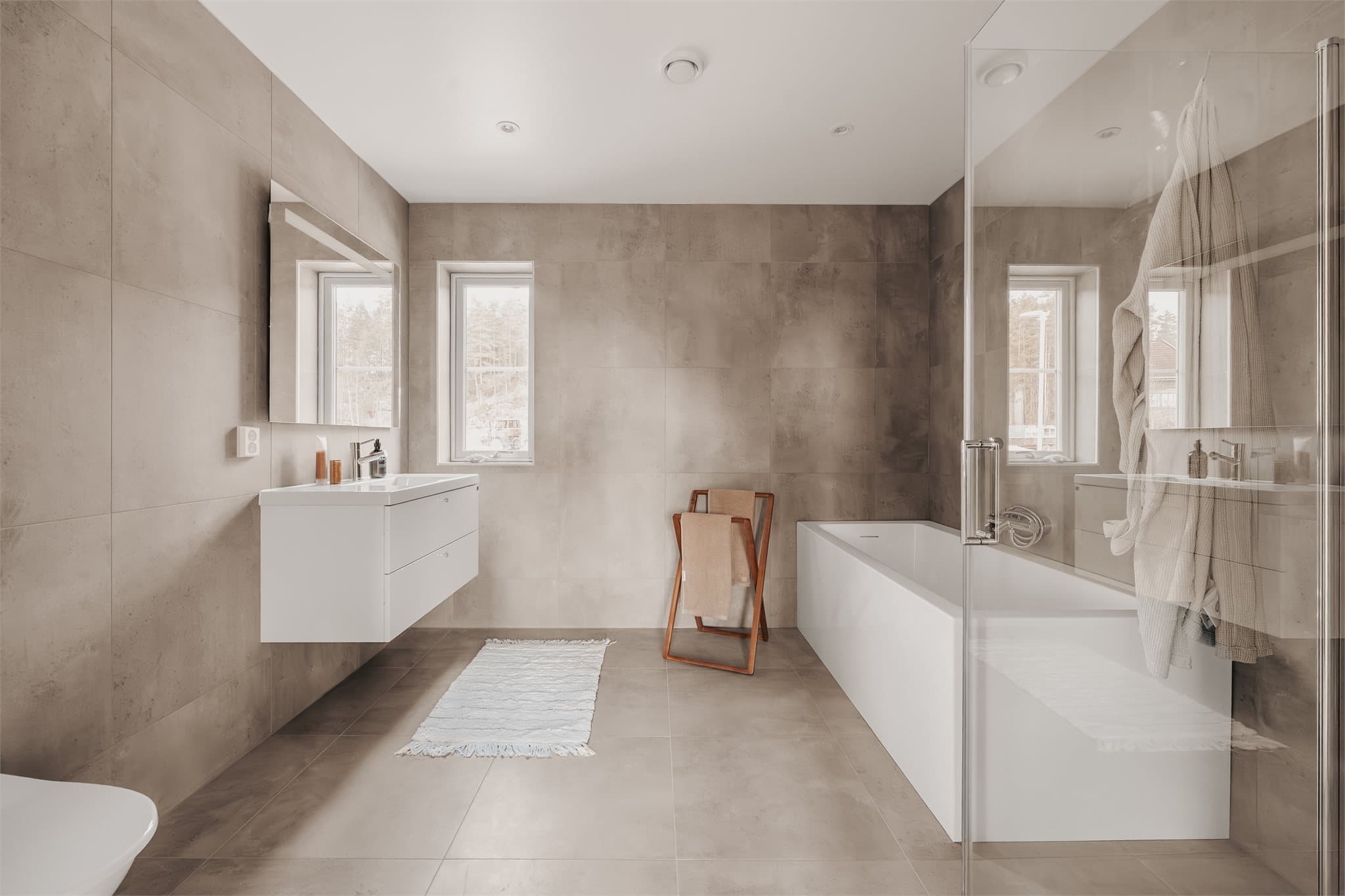 Delikat baderom med store, moderne fliser og påkostet badekar.
