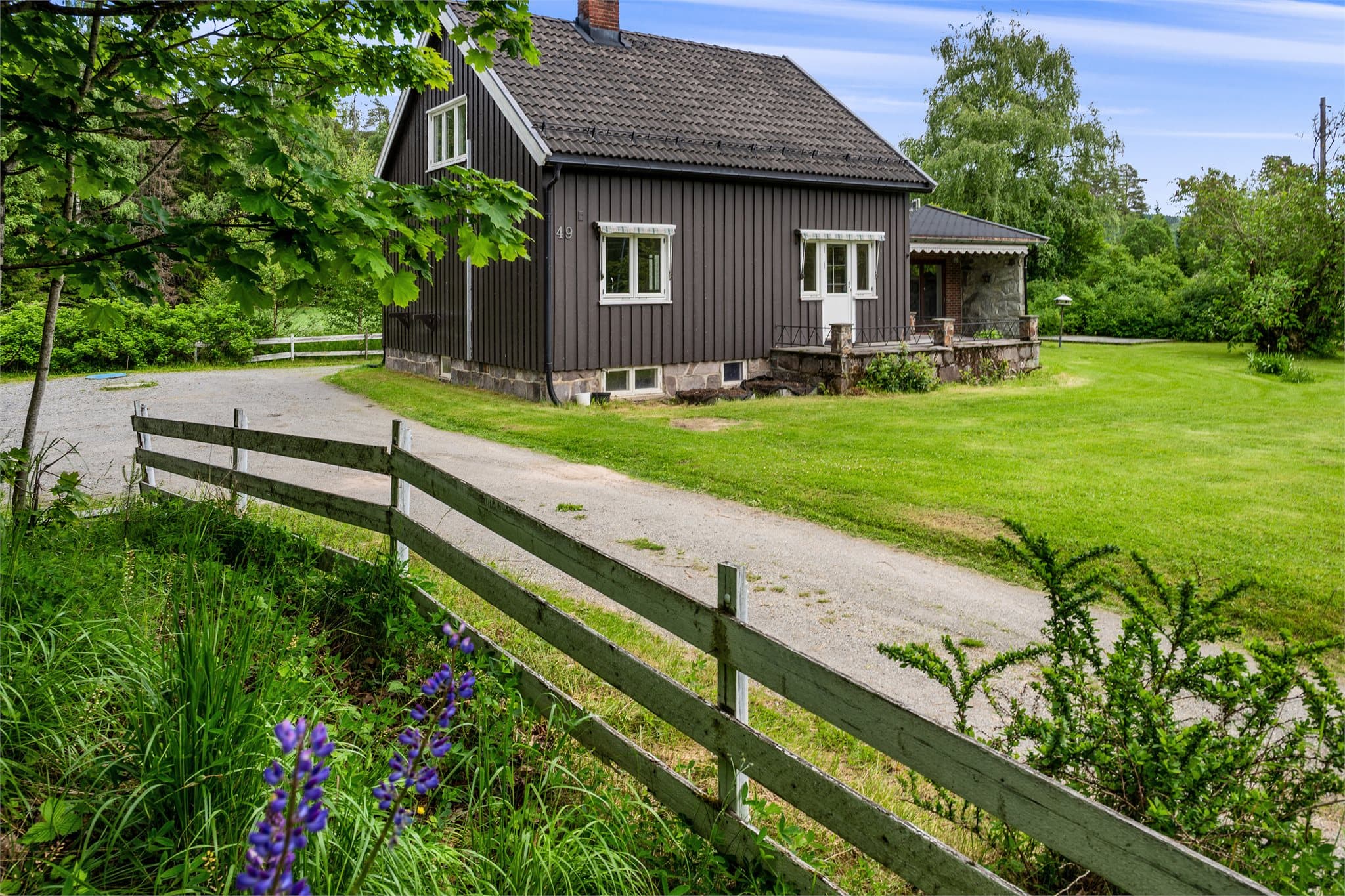 Innkjørselen slynger seg inn mot en sjarmerende bolig omgitt av en generøs hage med plass til både lek, dyrking og lange sommerdager utendørs.