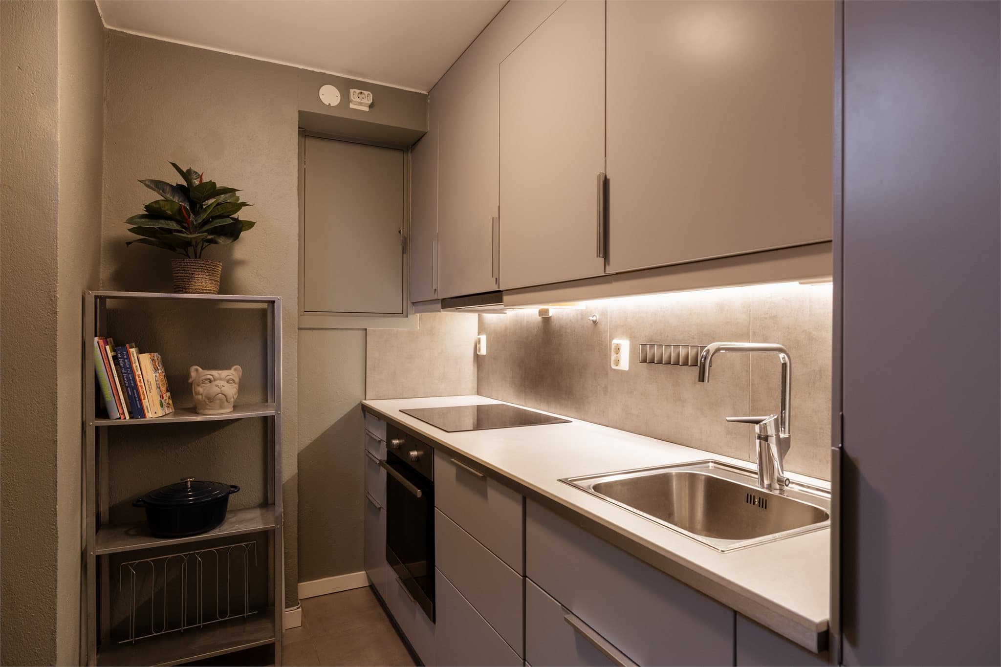 Hybelkjøkkenet har glatte fronter og en praktisk laminert benkeplate med nedfelt stålkum. Over benkeskapene er det fliser, og innredningen er komplett med integrert induksjonstopp, stekeovn, oppvaskmaskin og kjøl/frys.