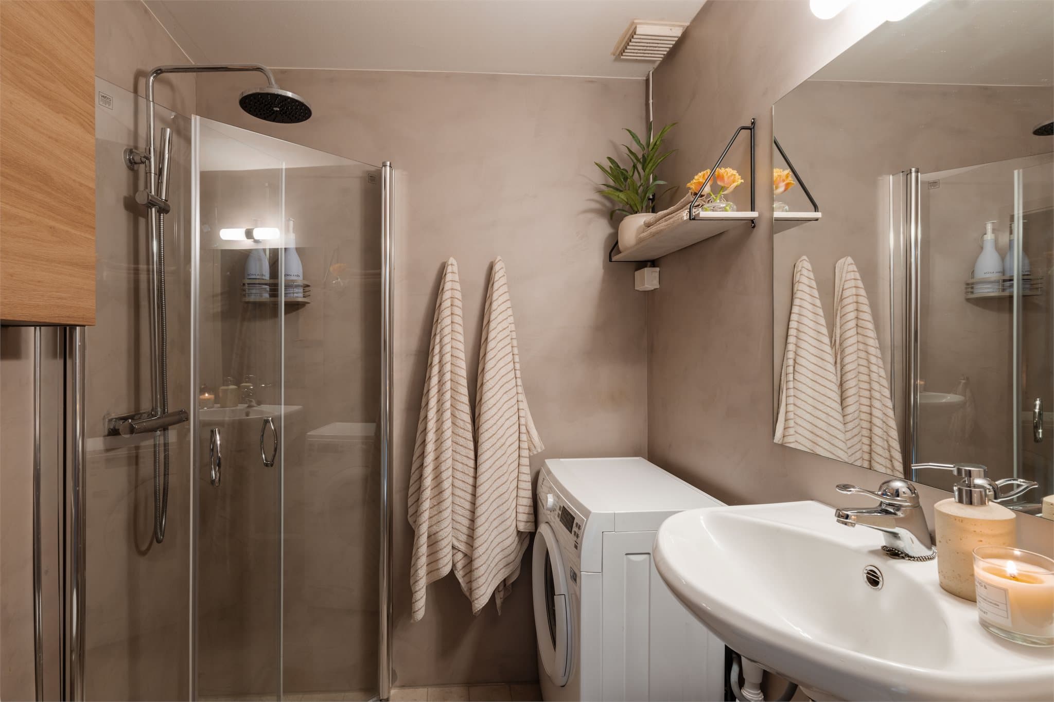 Baderommet har varmekabler i gulv, opplegg for vaskemaskin og svingbare glassdører som utnytter plassen effektivt.