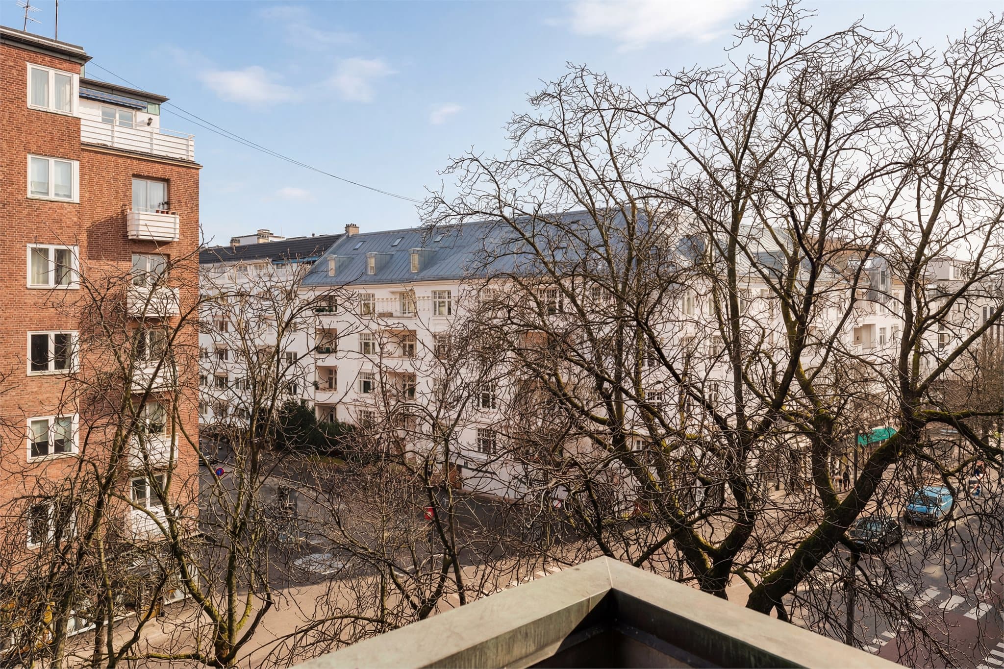 Utsikt mot nabolagets sjarmerende bygårdsarkitektur blant blomstrende trær om sommeren. Bildet er redigert med AI for å illustrere forholdene på solskinnsdager.