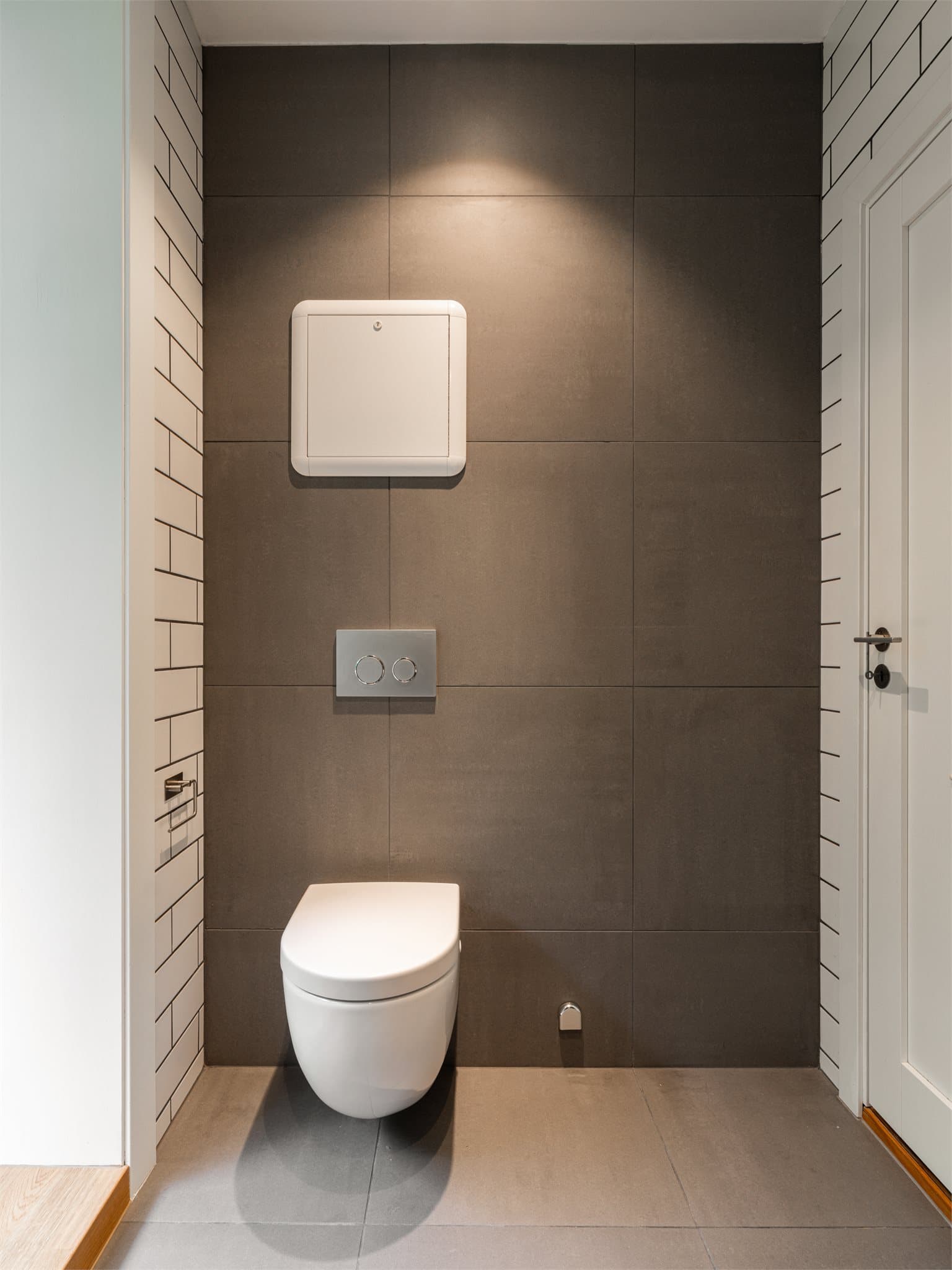 Badet har veggmontert toalett og moderne fliskombinasjoner på gulv og vegger.