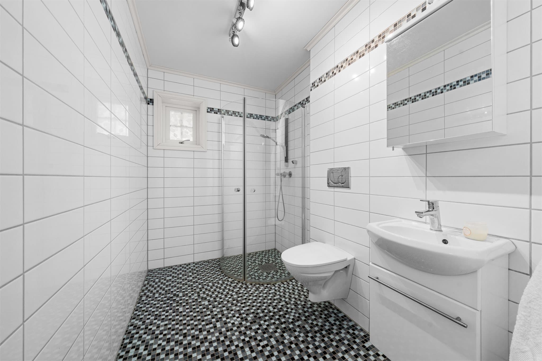 Baderom nummer to har dusjløsning, vegghengt toalett og servant på skapseksjon.