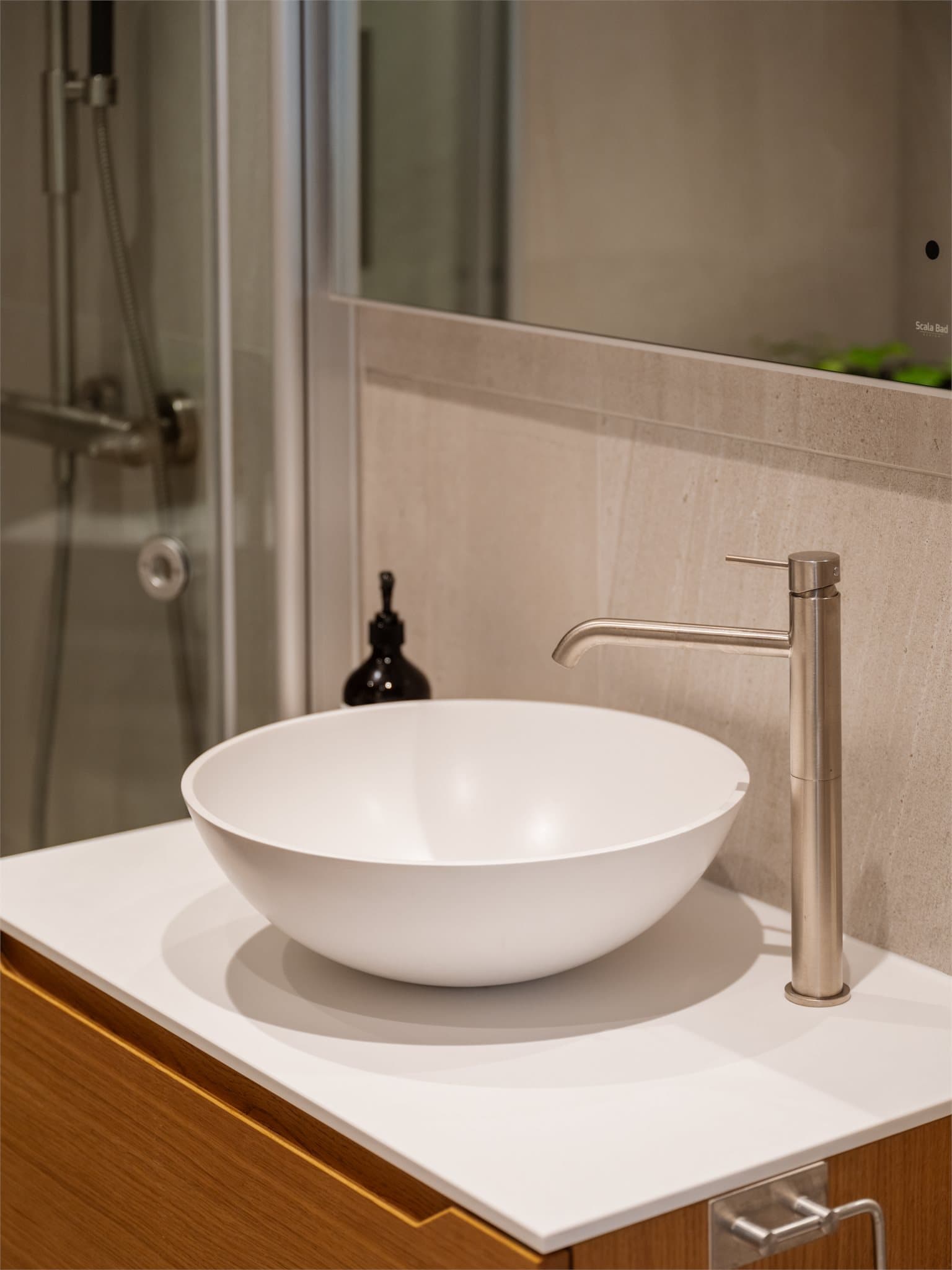 Badet er utstyrt med dusjhjørne, vegghengt toalett og stilren servantinnredning.