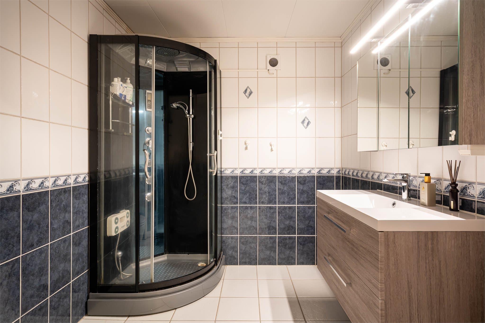 Badet har flislagte vegger og gulv i lyse og mørke toner.