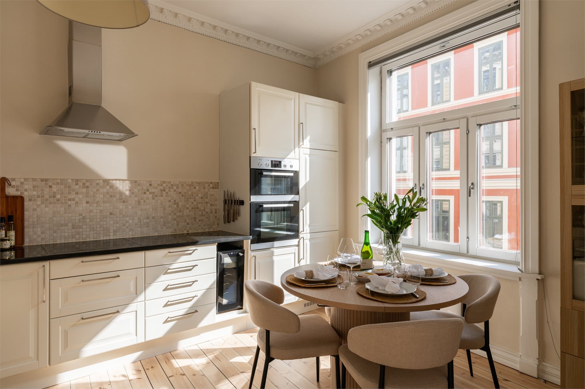 Kjøkkeninnredningen har profilerte fronter i klassisk stil, harmonisk tilpasset leilighetens arkitektur og uttrykk. Benkeplate i steinmateriale gir gode arbeidsflater, og mosaikkfliser over benken tilfører et eksklusivt preg.