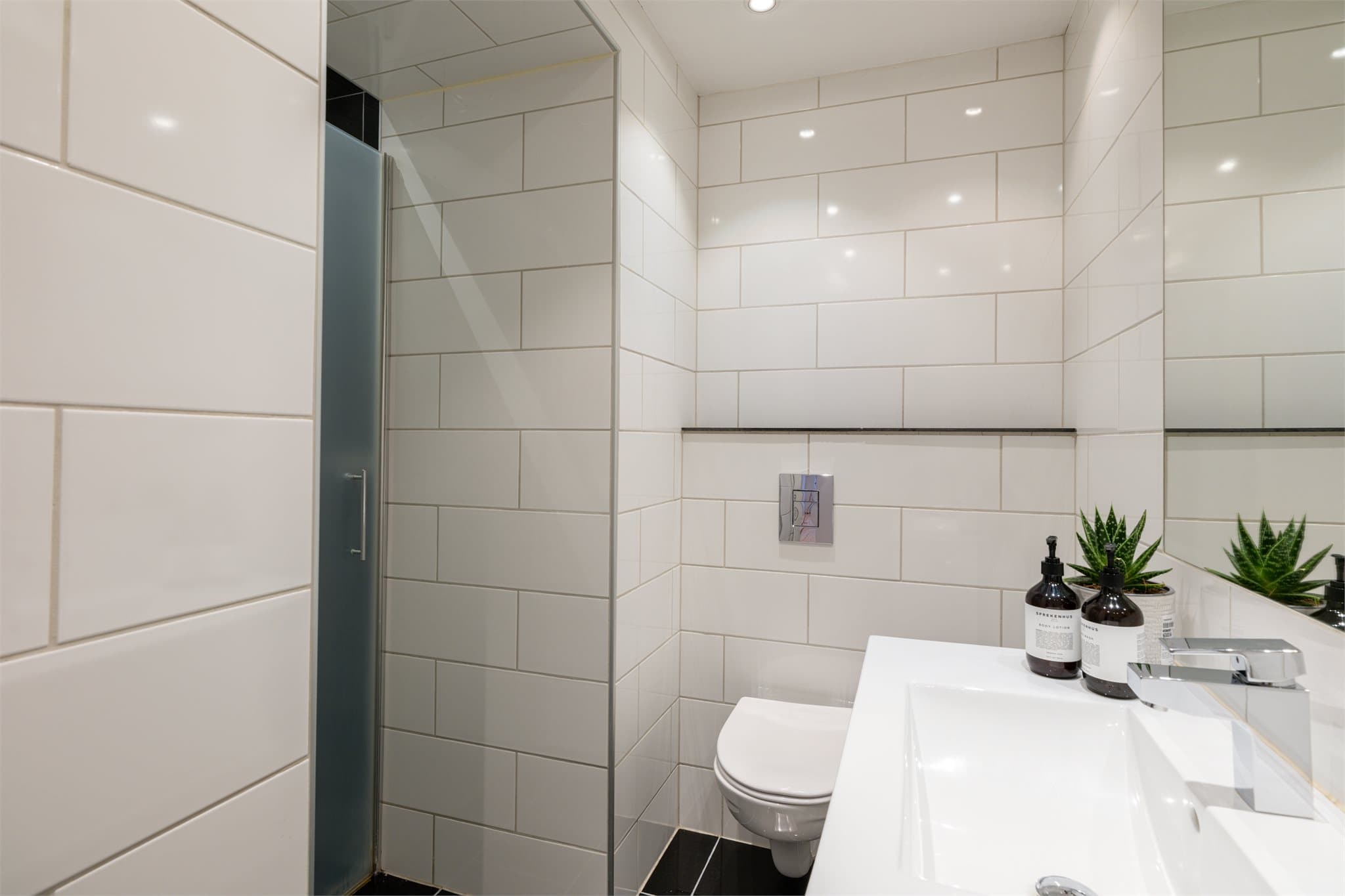 Badet har innfelte downlights i taket og er innredet med vegghengt toalett, servant nedfelt i moderne baderomsinnredning samt dusjhjørne med svingbare glassdører.