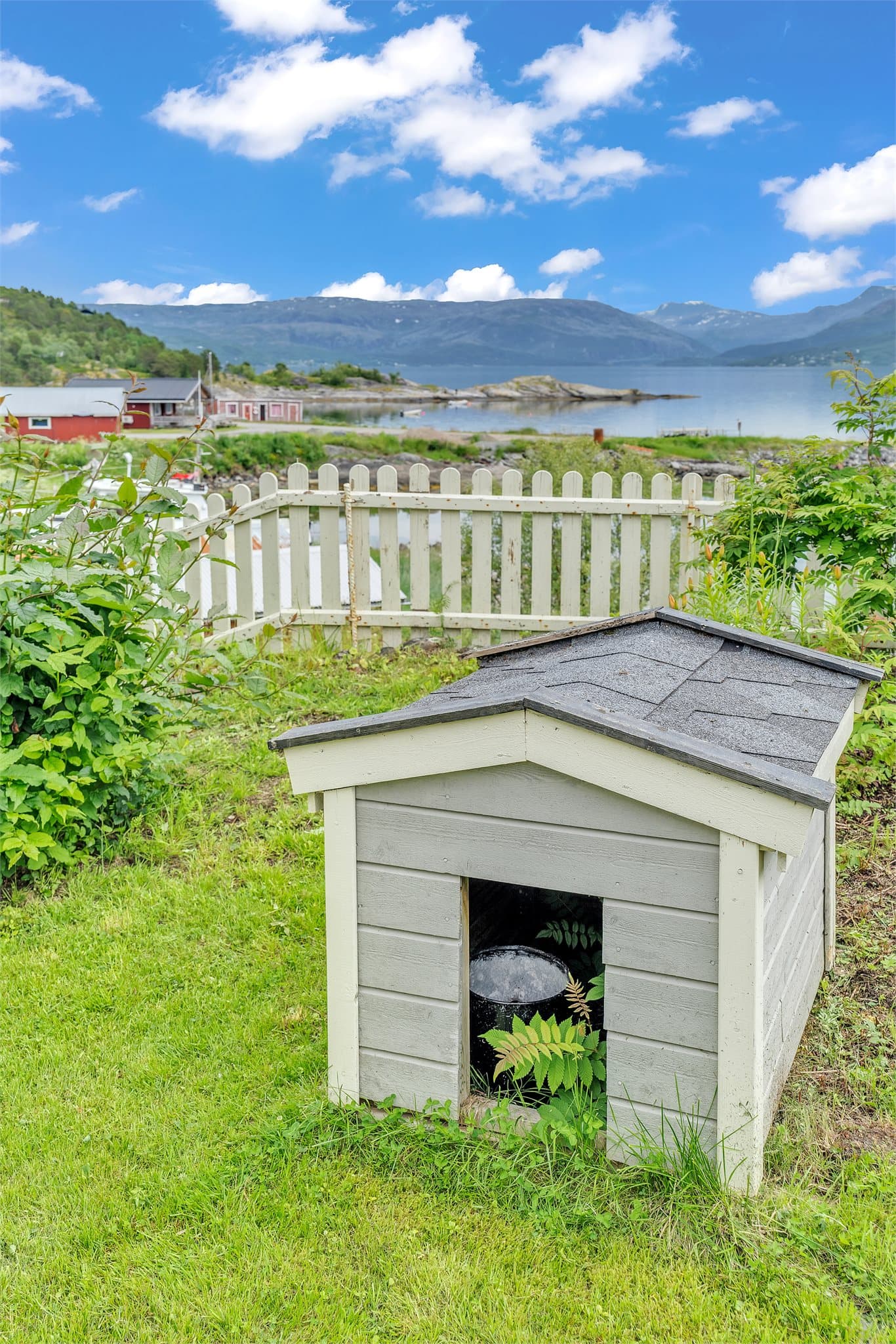 Stor hage med plen og beplantning, med utsikt mot sjøen.