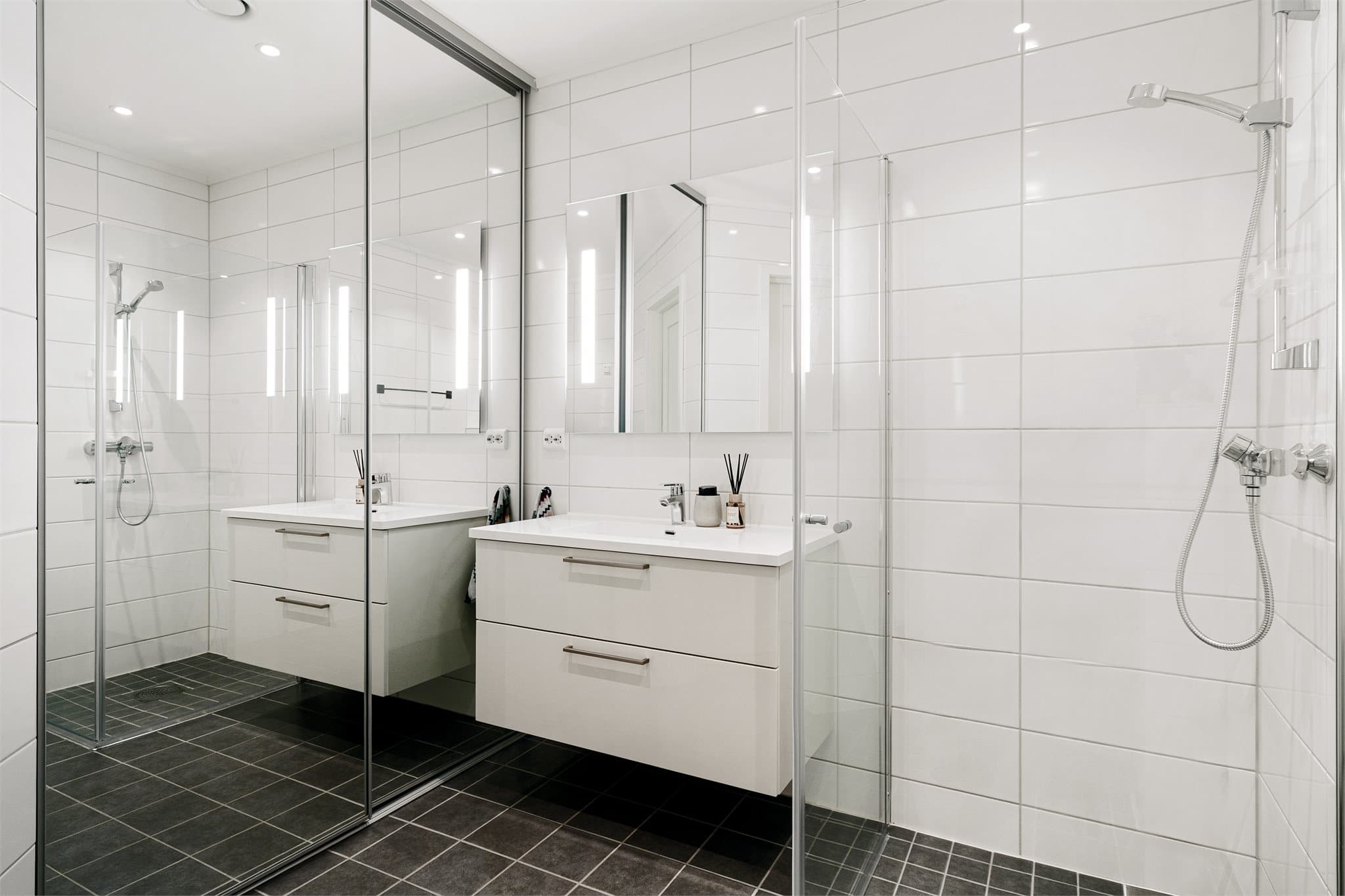 Badet er utstyrt med dusjvegger, vegghengt toalett og baderomsinnredning med heldekkende servant.